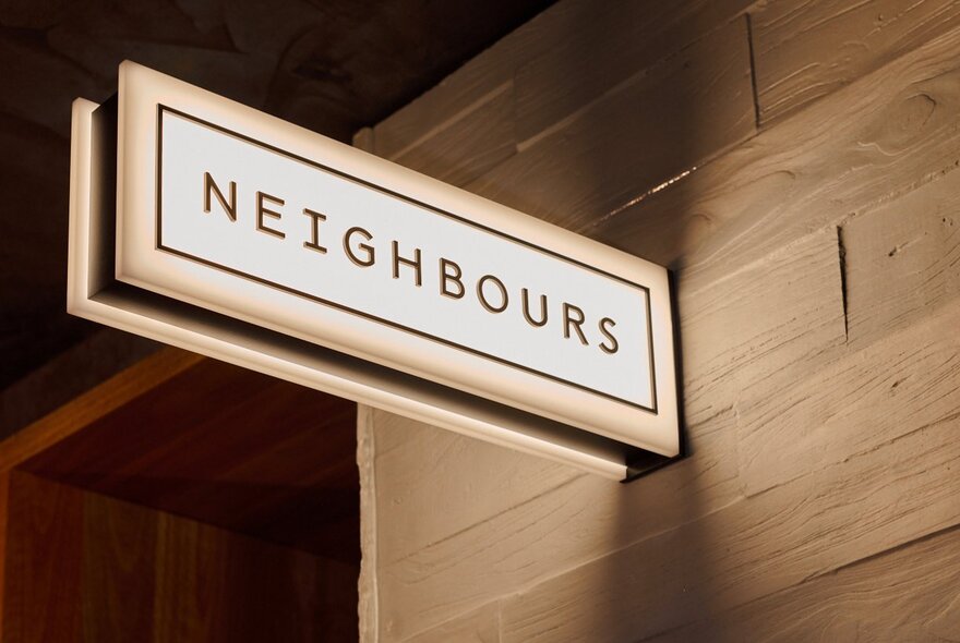 An illumated sign on a wall saying 'Neighbours'.