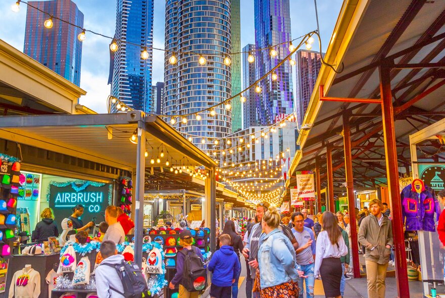 Crowds in a market in the city with festoon lights.