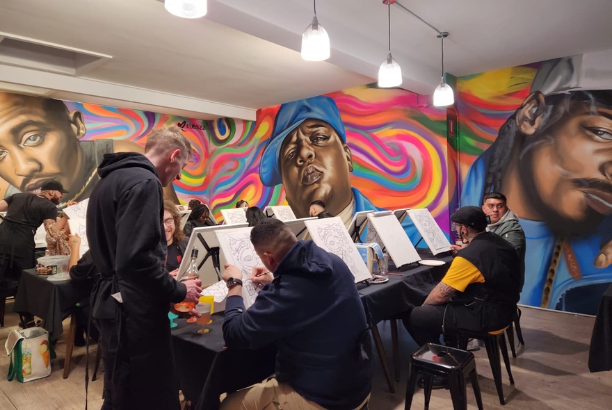 Several rows of people painting on canvases in a room with large, wall murals.