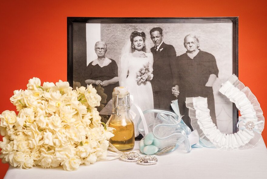 A vintage framed wedding photo dating from the 1960s resting on a table with a bouquet of white flowers, and wedding day souvenirs.