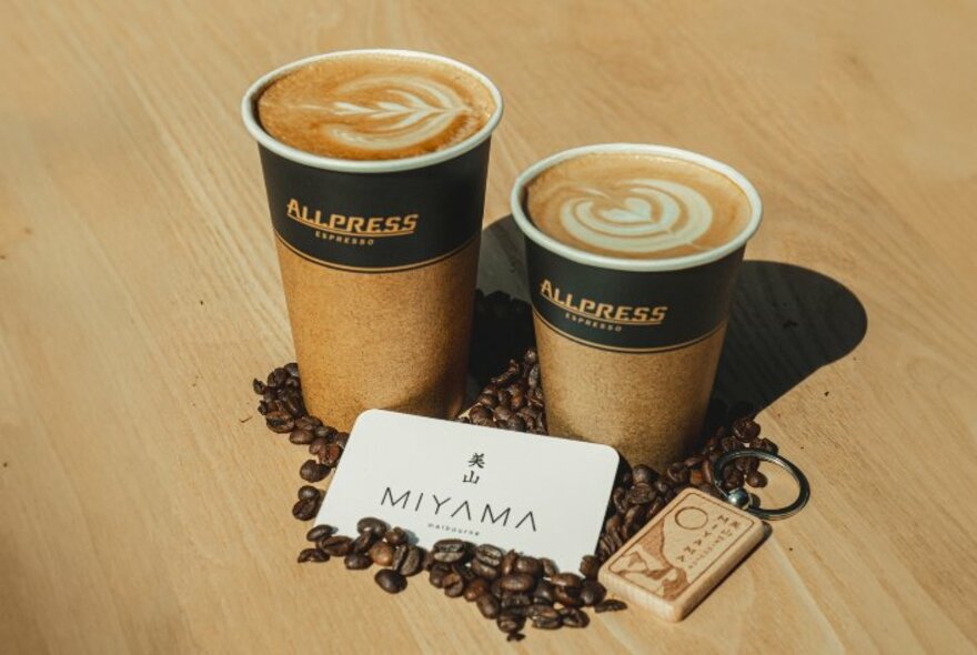 A small and large takeaway coffee coffee, with a business card and coffee beans on a wooden table.