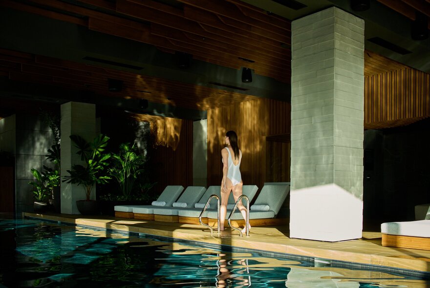 Woman walking past a hotel pool with lounge seating and dappled light.