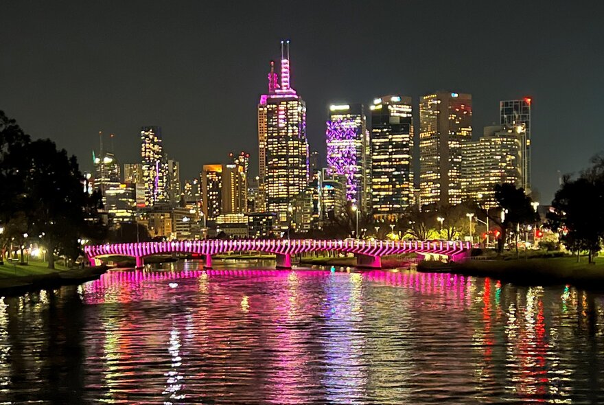 Melbourne's cityscape at night featuring a brightly lit skyline reflecting off the wide Yarra wide river in the foreground.