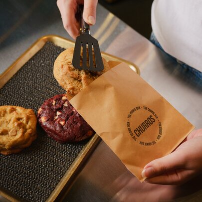 Hands sliding cookies into a branded paper bag.