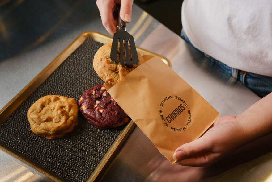 Hands sliding cookies into a branded paper bag.