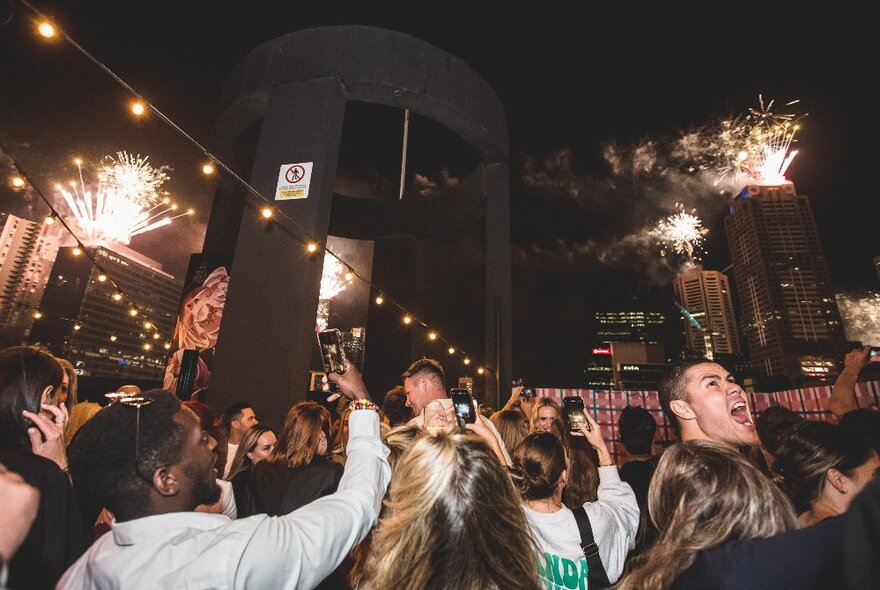 Revellers enjoying a rooftop nightclub on New Year's Eve while fireworks go off in the background. 