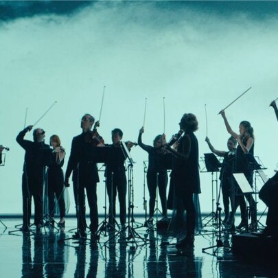 Silhouettes of an orchestra on stage, performers standing, violin bows in the air. 