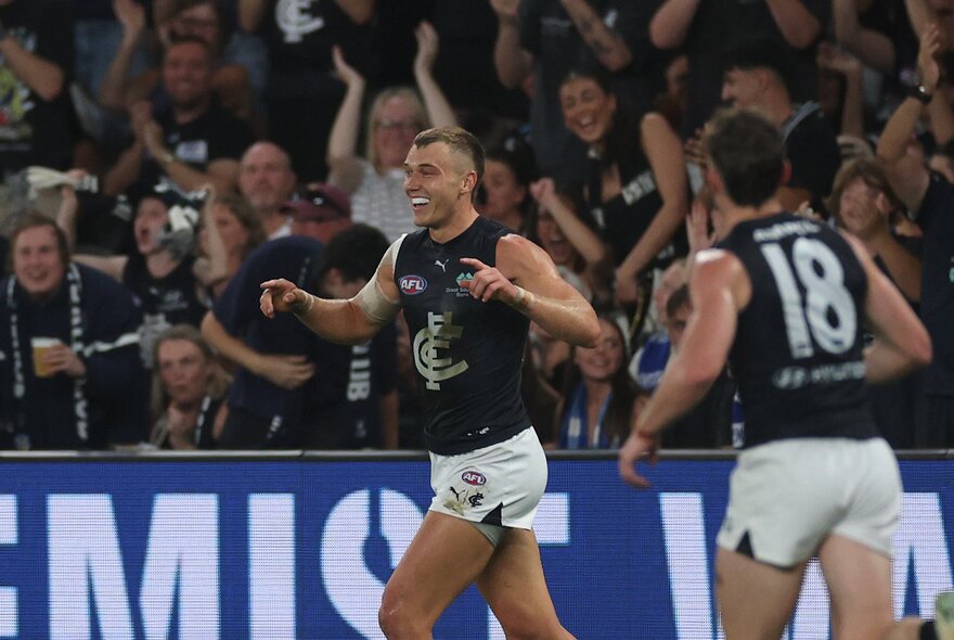 Carlton AFL  players celebrating during a match, the fans cheering in the stadium behind them.