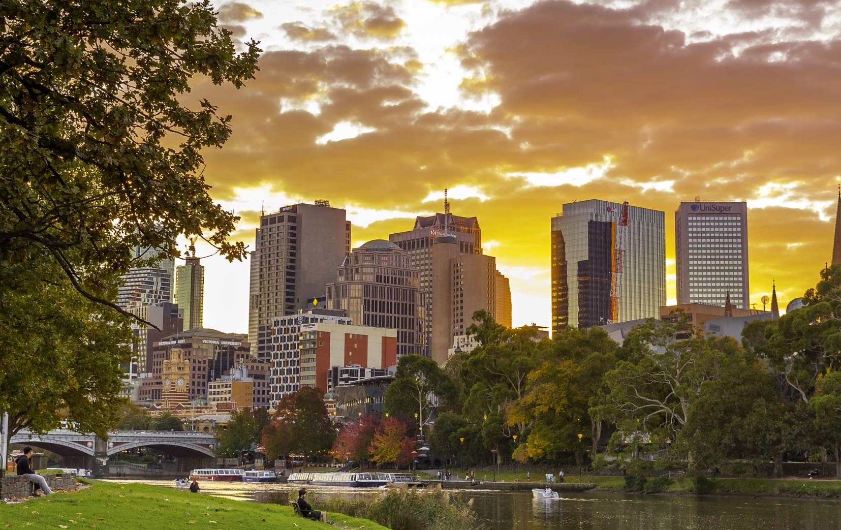 People sitting on the grass by the Yarra River watching the sunset.