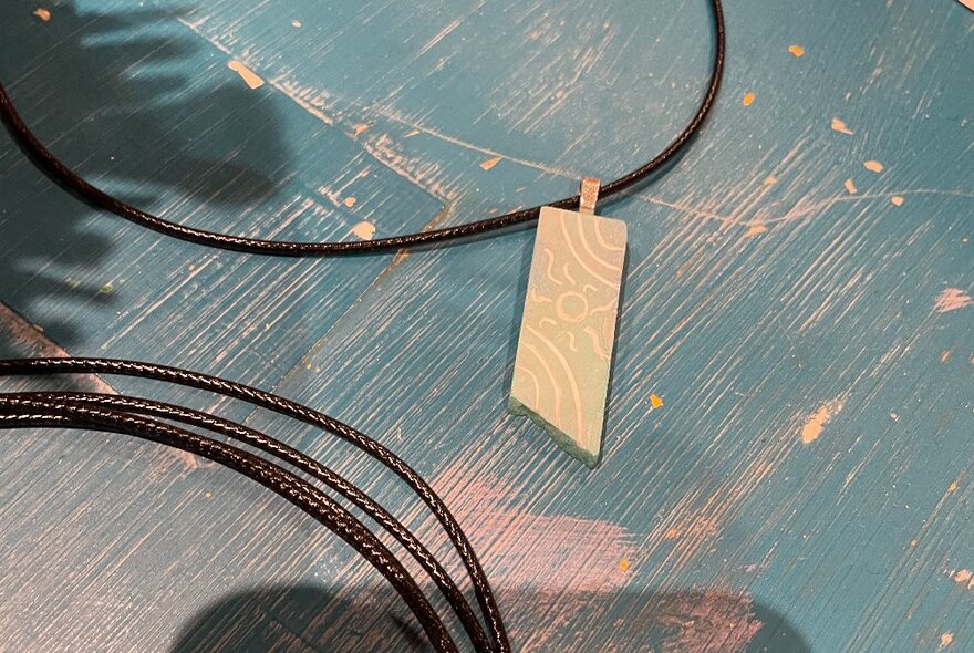 A rectangular pendant carved from soapstone on a thin leather strap.