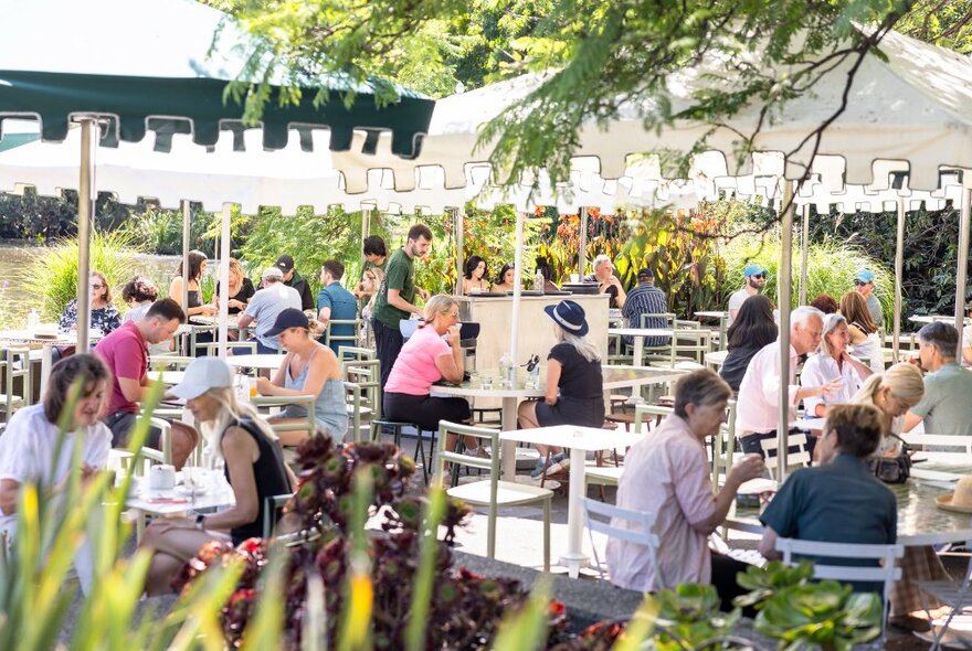 People gathered at tables in an outdoor eating area wiht umbrellas.