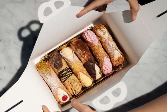 A person opening a tasting box with six different cannoli inside.