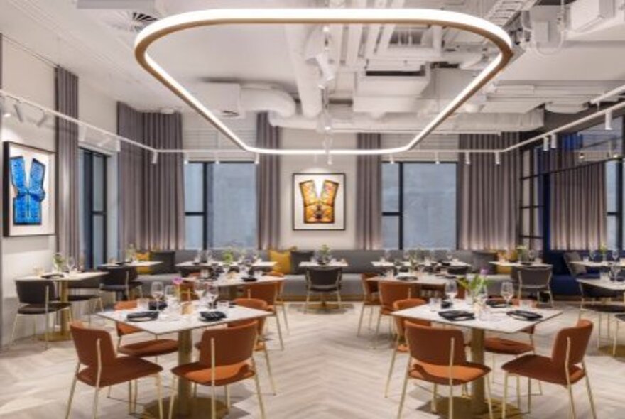 The modern interior of a restaurant with widely spaced square tables and bench seating along the back windows.