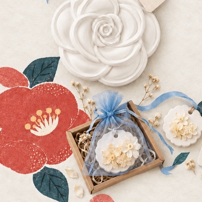 A set of white flower-shaped plaster aroma diffusers packaged in a small gift box alongside a red camellia graphic.