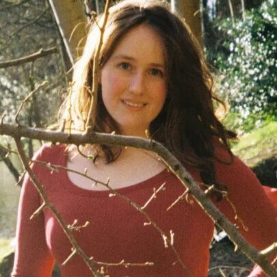 A woman standing outdoors surrounded by foliage.