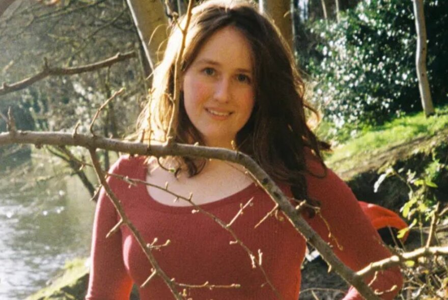 A woman standing outdoors surrounded by foliage.