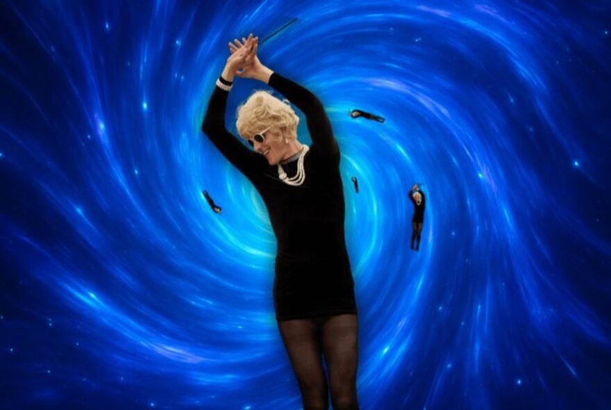 An older woman with blonde hair, sunglasses and jewellery, wearing black, dancing in a blue painted spiral backdrop.