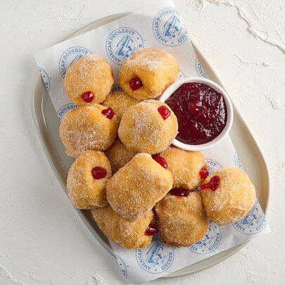 A platter of ten hot jam doughnuts with a condiment bowl filled with extra jam.