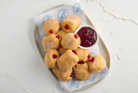 A platter of ten hot jam doughnuts with a condiment bowl filled with extra jam.