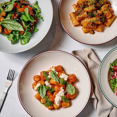 Four round plates on a marble table, one with a roast pumpkin salad, one with a rigatoni bolognese, one with a tomato gnocchi and one with a radicchio salad.