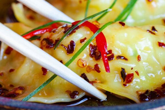 A close up of chilli flakes on a dumpling and chopsticks poised to pick it up.