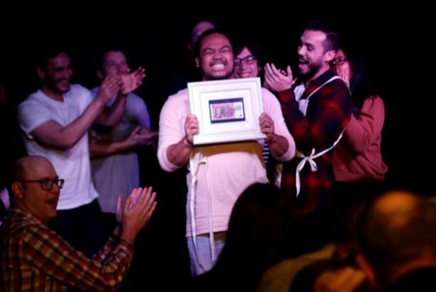 Person holding a certificate, being applauded by onlookers.