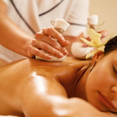A woman having a deep tissue massage from a therapist who is using two white compresses. 