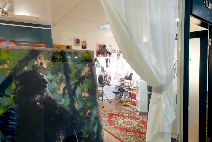 A gallery space with a sheer white curtain pulled aside and artwork on the floor. 
