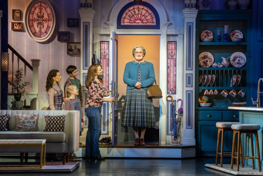 A scene from Mrs Doubtfire The Musical showing Mrs Doubtfire in a doorway and kids inside the entrance of a living room. 