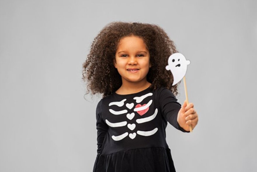 A child wearing a black dress with rib bone decoration, holding a ghost on a stick.