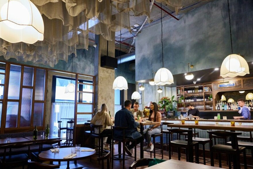 People dining on high tables in a glamourous restaurant with pendant lights.