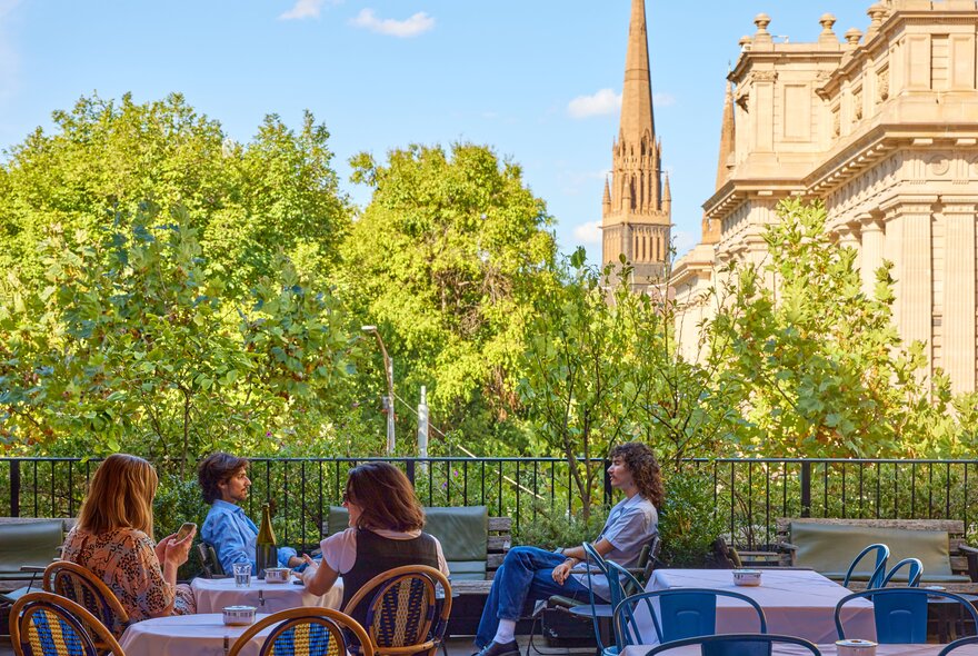 Four people sitting at a rooftop bar with a view of trees, a cathedral and a heritage building.