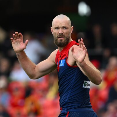 A Melbourne Demons AFL player with his hands up in the middle of the ground during a game.