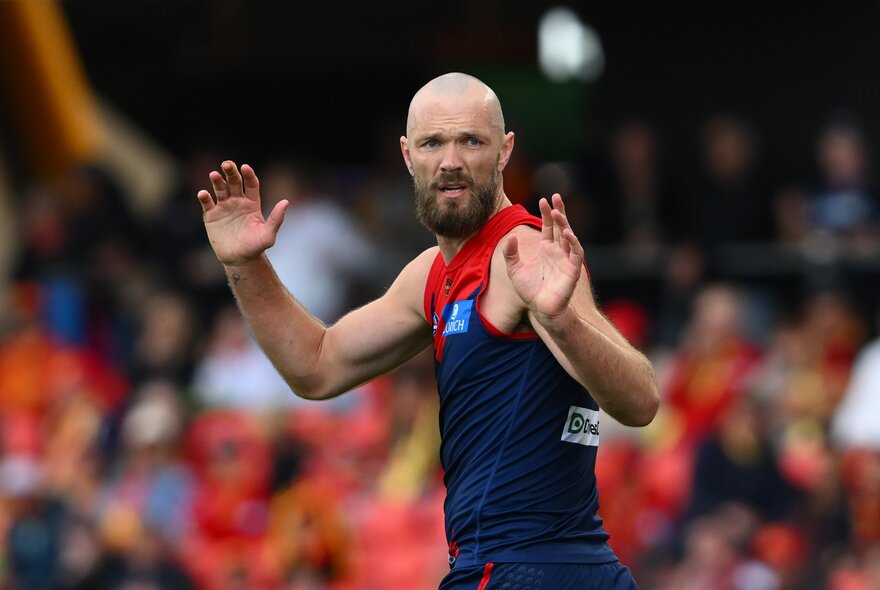 A Melbourne Demons AFL player with his hands up in the middle of the ground during a game.