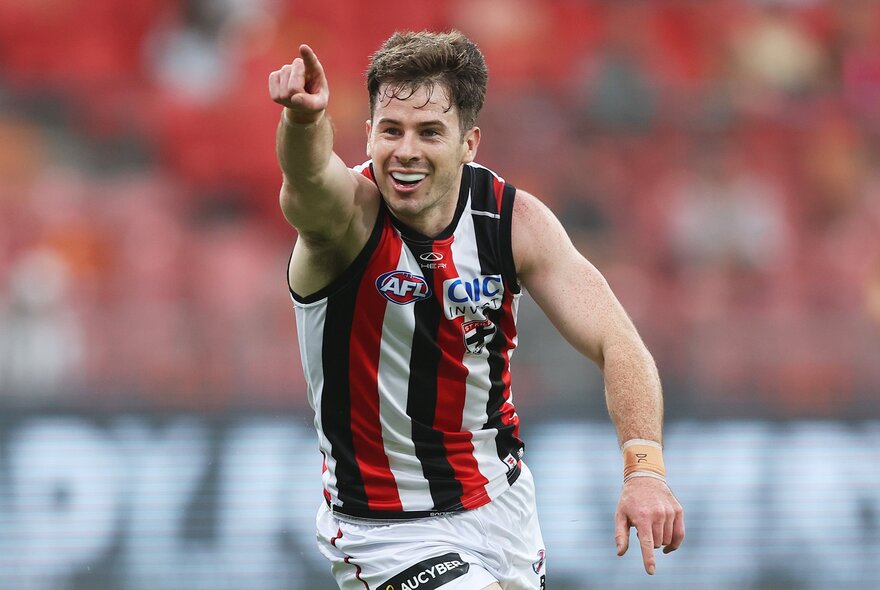 A St Kilda AFL player celebrating on the field with one of his arms raised with his finger pointing.