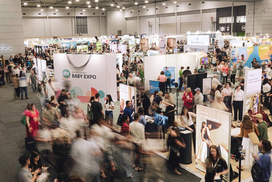 Looking down on a pregnancy and baby expo with many people moving around near booths. 