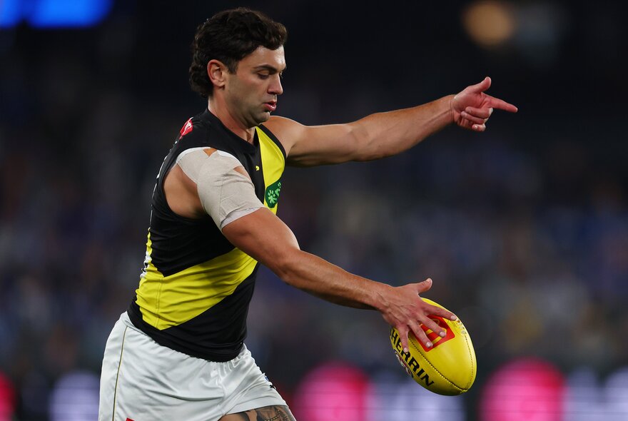 A Richmond AFL football player about to kick the football on the field during a match.