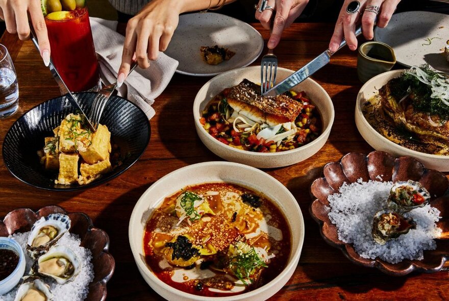 A selection of tasty dishes, with two people using cutlery to serve up two of them.