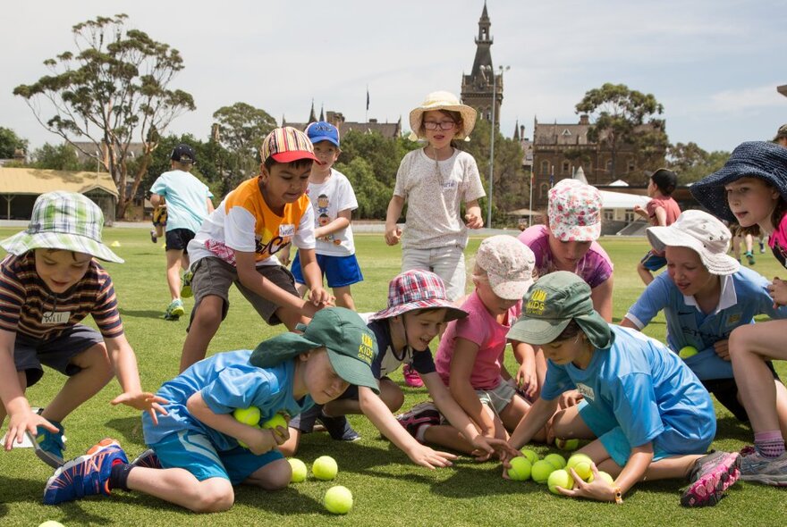 Group of primary school-aged children playing with tennis balls on a green lawn.