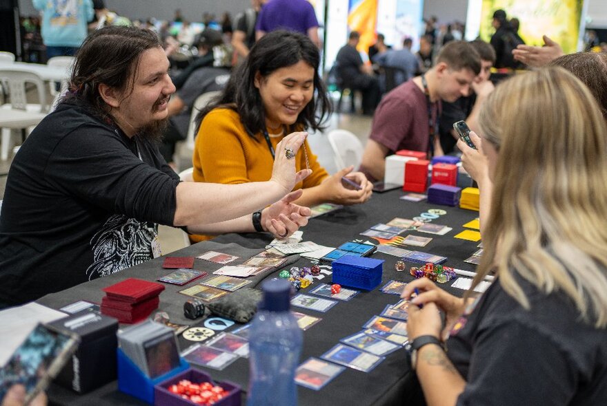 People playing trading card games at a table at a games expo.