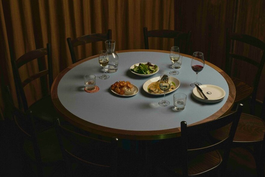 A dimly lit circular table with a selection of Italian dishes, with an empty plate, wine glasses and cutlery.