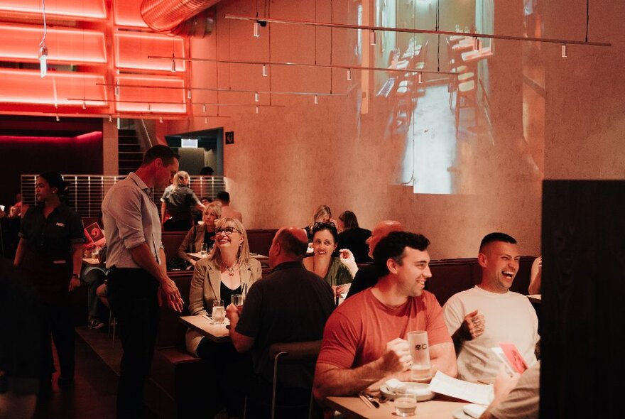 Diners seated at tables in a restaurant with shiny white walls and red lighting.