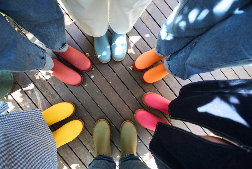 Looking down at the feet of six people, all wearing brightly coloured Merry People rubber boots.