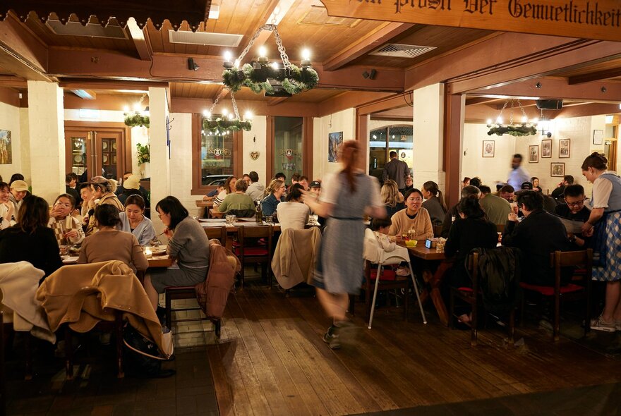 Seated customers dining in a German restaurant with woodwork and wooden chandelier.