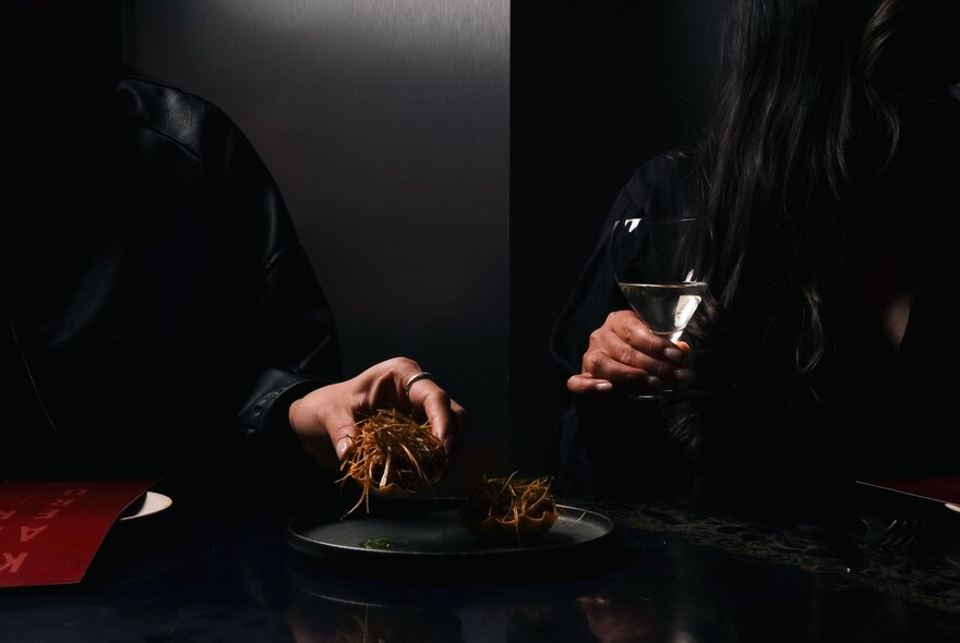 Hands holding drink glasses in a dark room.