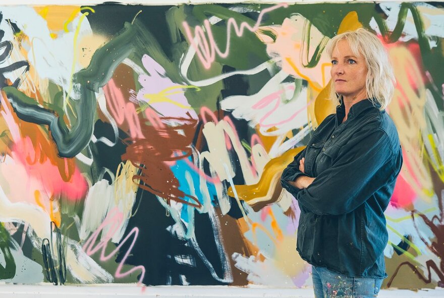 Artist standing in front of an abstract artwork, with arms folded.