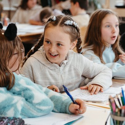 Primary school aged children seated at a large table writing and interacting during a creative writing workshop in a bright studio space.