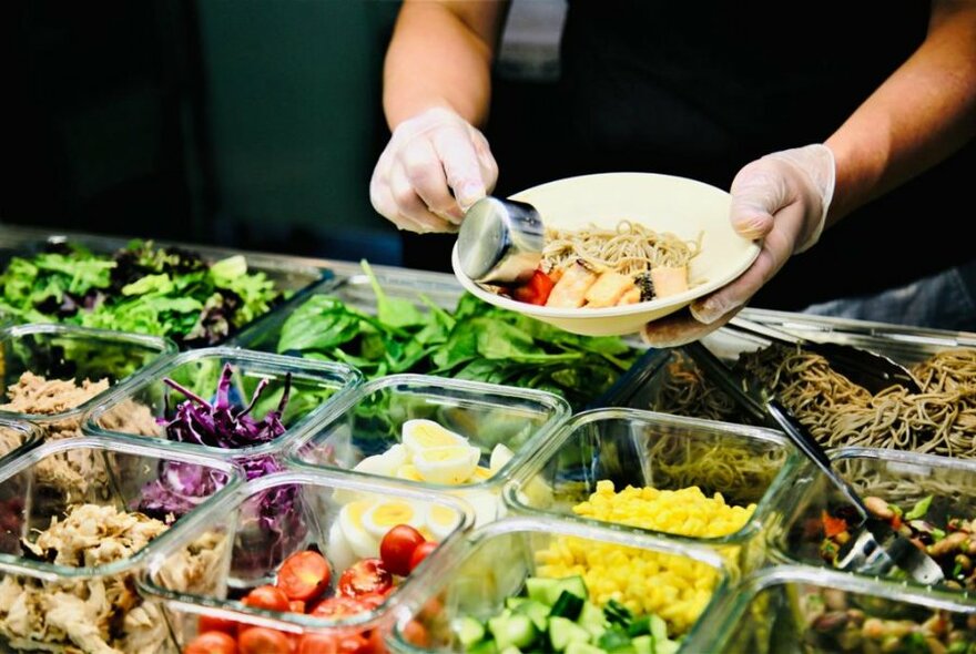 Salad being prepared from bowls of chopped vegetables.