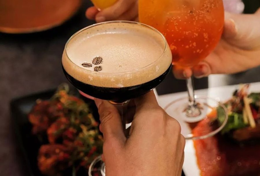 A hand holding an espresso martini over a table