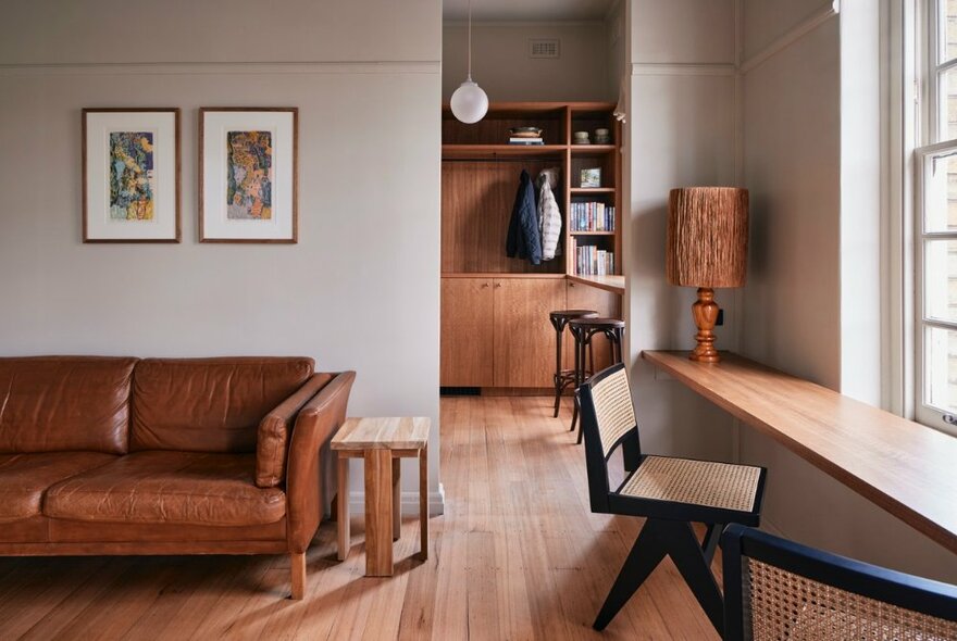 A comfortable sitting room inthe suite at The Courthouse Hotel, with modernist decor and furnishings, including a leather couch, wooden desk and chair facing a window, bookshelf and lamp.